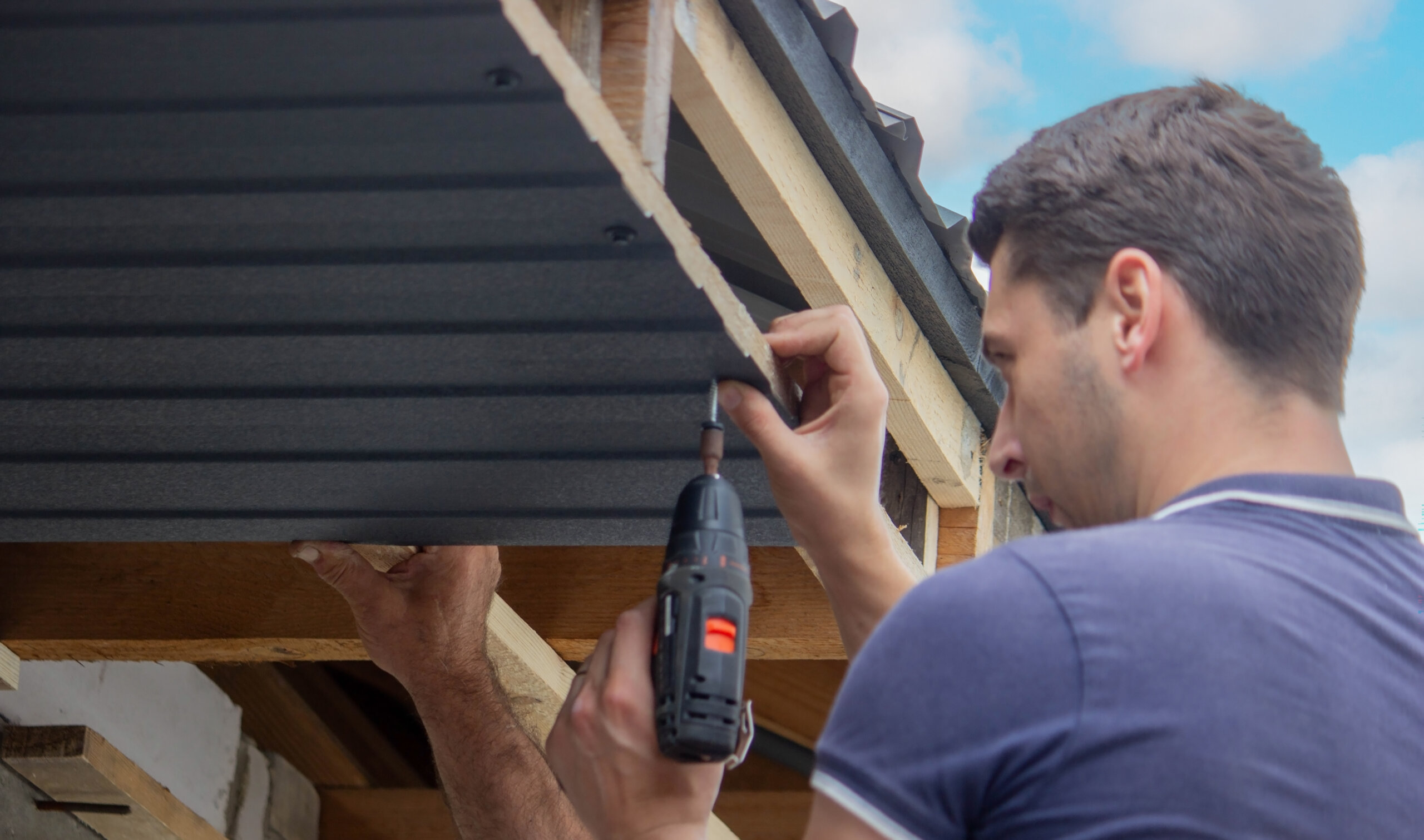 a man repairs the roof, tightens the self-tapping screw with a screwdriver.